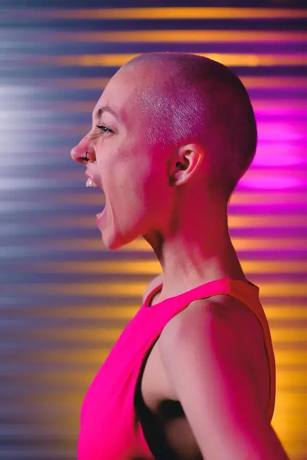 A bald woman in pink with an expression of shouting in studio